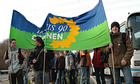 Demonstrationsteilnehmer vor Reisebus tragen ein großes Transparent mit dem GRÜNEN Parteilogo
